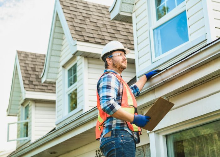 man with hard hat standing on steps inspecting house roof